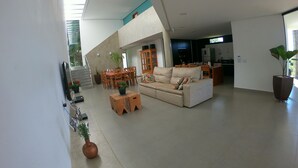 Amplia sala de estar con techo alto, un sofá, una mesa de comedor y una cocina al fondo.