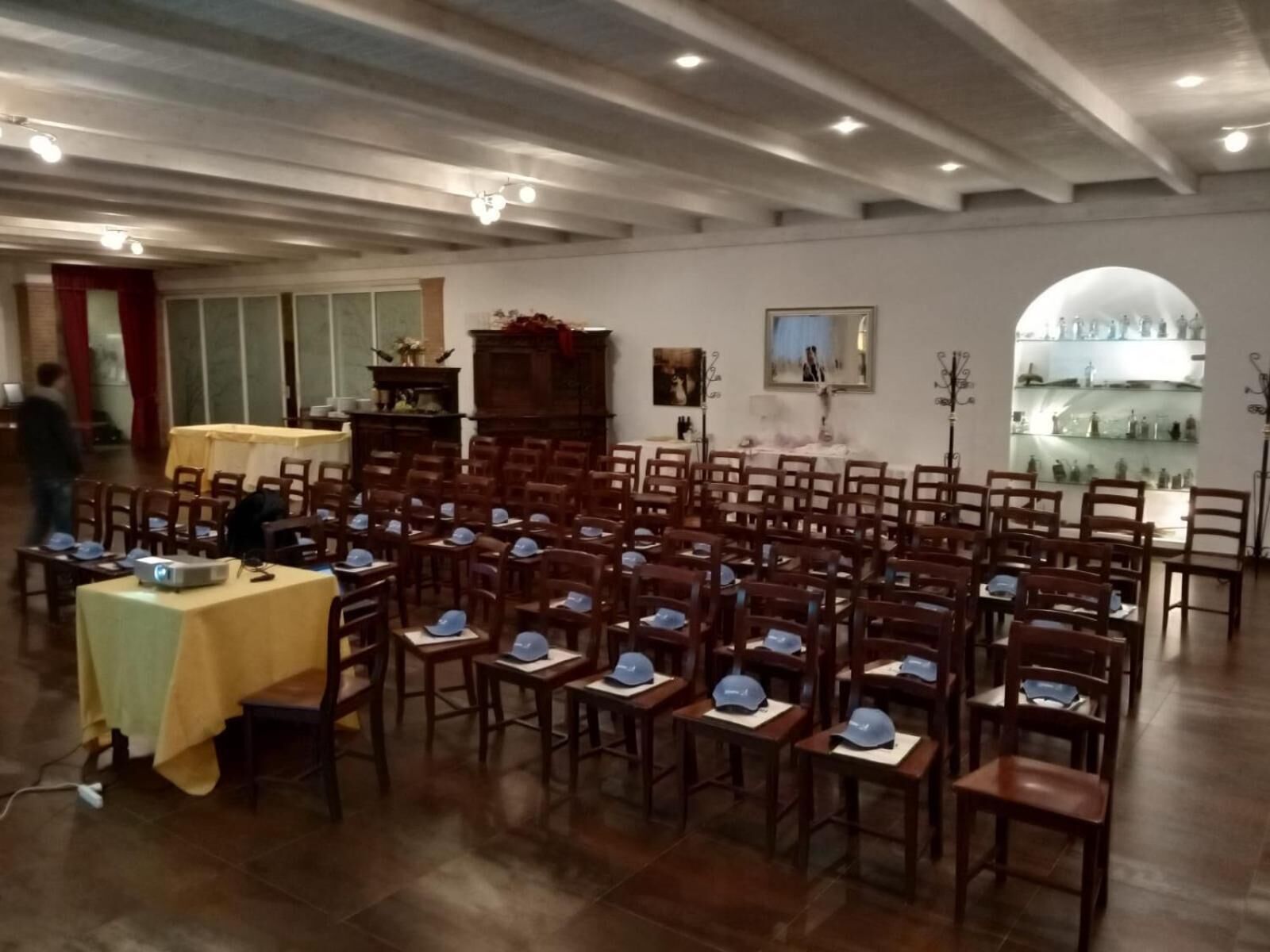 A conference room with rows of wooden chairs, a projector on a table, and a large window.