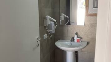 Uma casa de banho com lavatório pedestal branco, um espelho em cima e um secador de cabelo na parede.