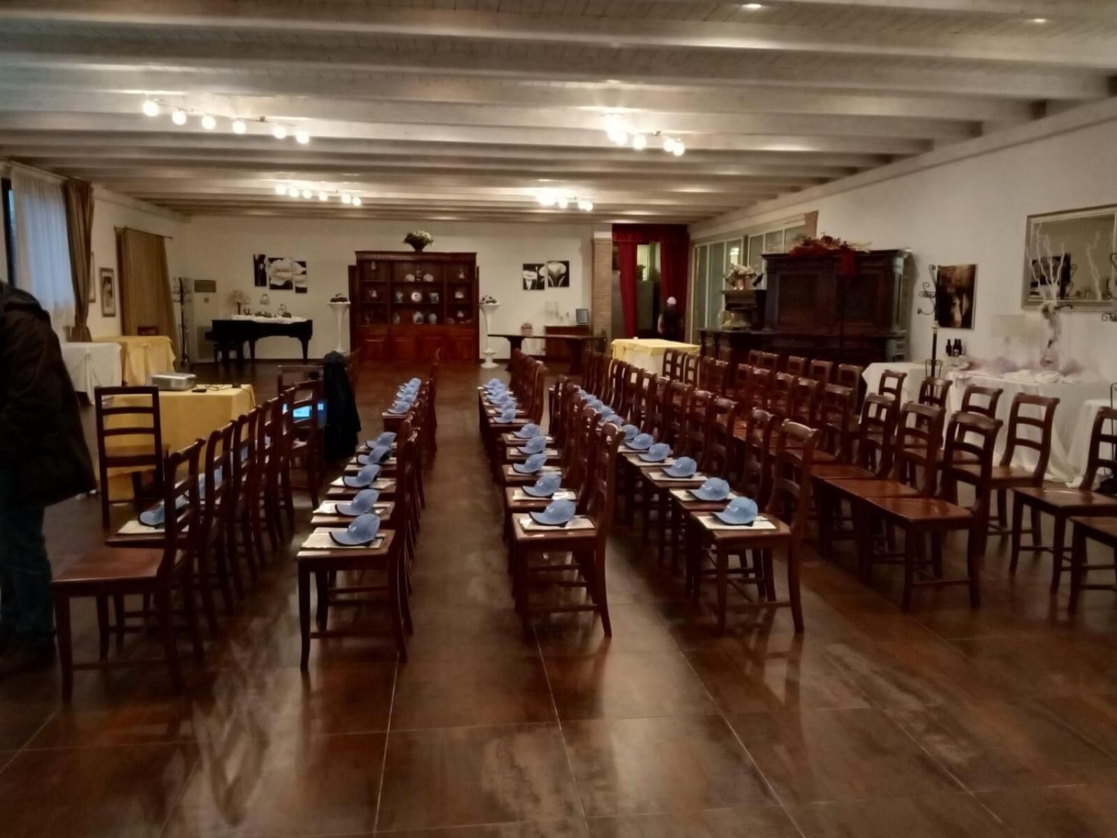 A long dining hall with rows of tables and chairs, wooden floors, and a high ceiling with exposed beams.