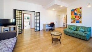 Una sala moderna con un sofá, un televisor, una mesa de centro de cristal y un cuadro abstracto y colorido en la pared.