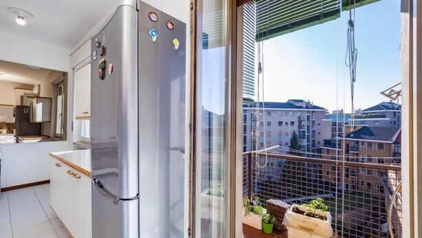 Una cocina moderna con refrigerador de acero inoxidable, encimera de madera y vistas a un balcón con plantas en macetas.