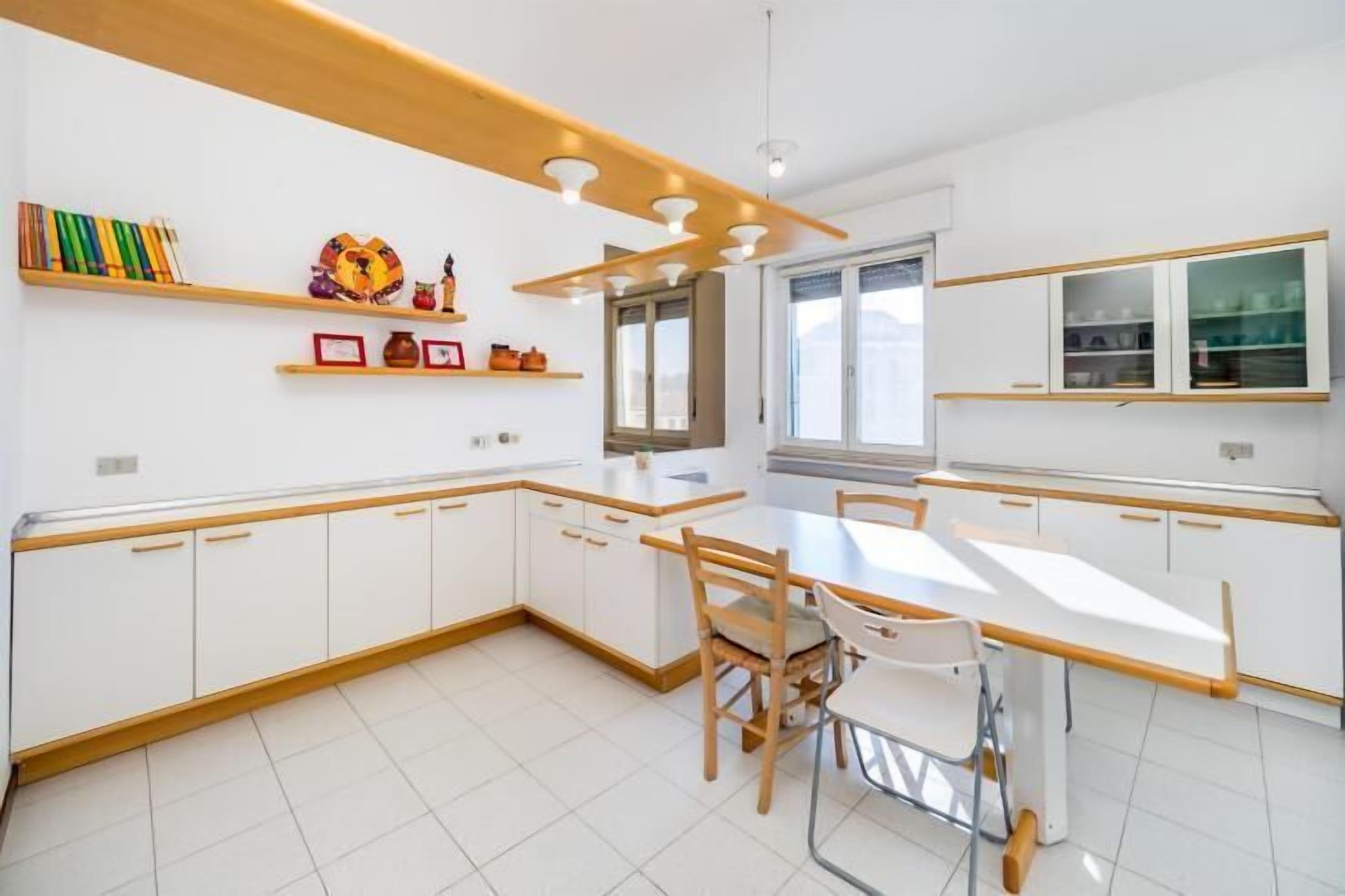 Une cuisine moderne avec des meubles blancs, des plans de travail en bois et un coin repas comprenant une table et des chaises.