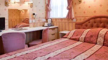 A hotel room with a bed, a desk, a chair, a mirror, and a window with curtains.