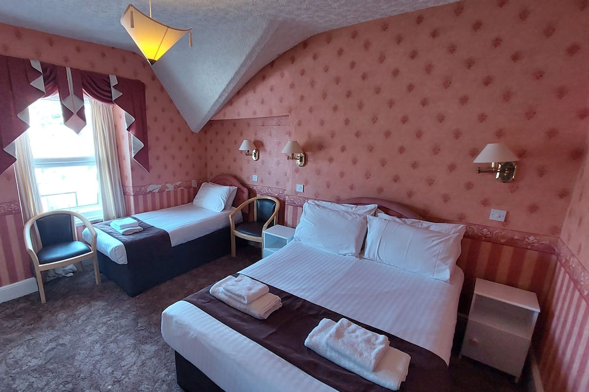 A hotel room with two beds, a chair, a small table, and a lamp.