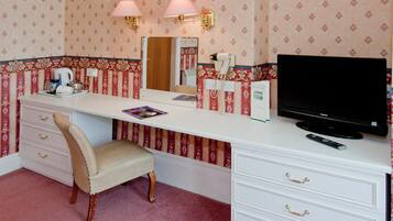 Habitación de hotel con un escritorio blanco, televisor, silla, espejo y teléfono.