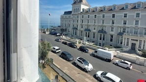 Vista de una calle con coches aparcados y un edificio alto de arquitectura clásica.