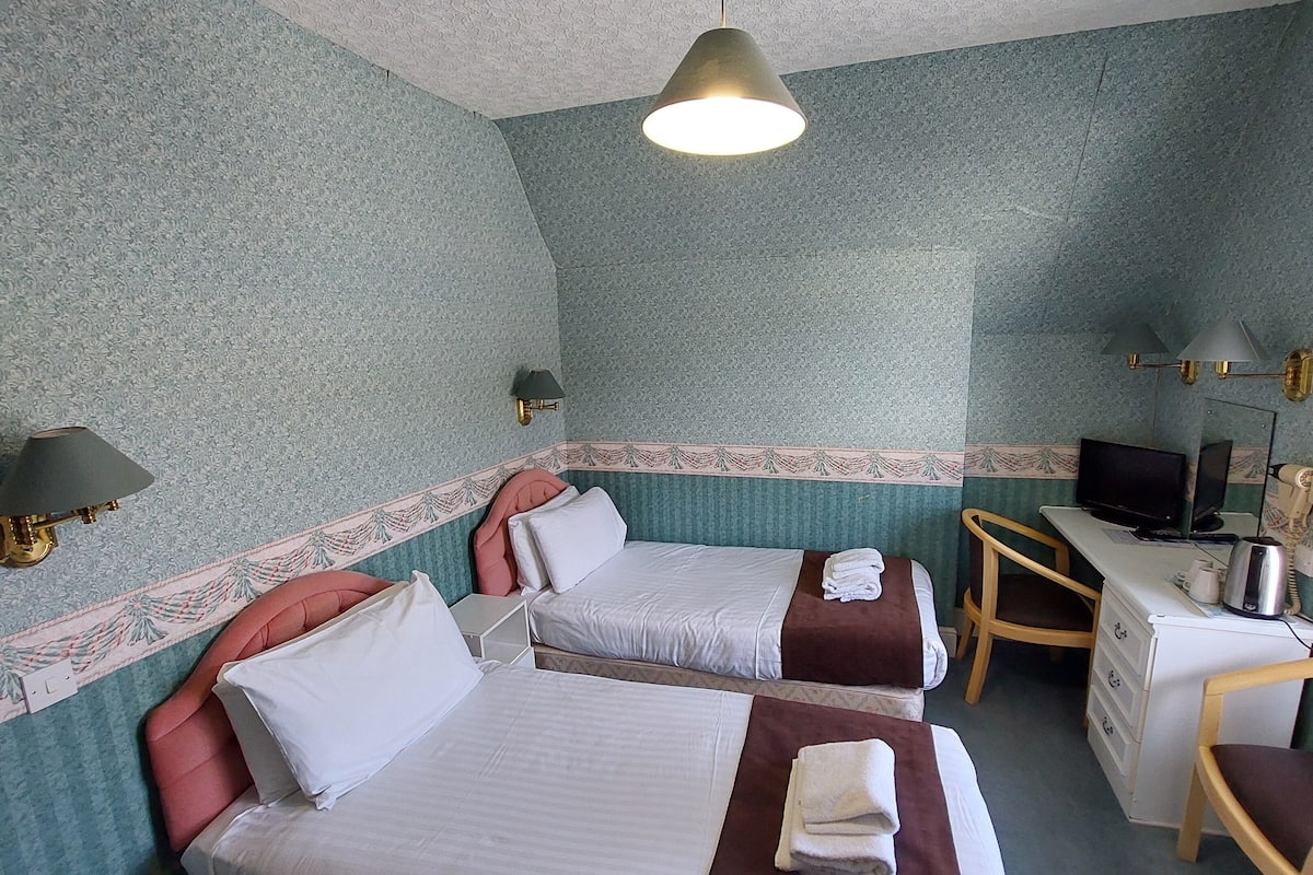 A hotel room with two beds, a desk with a computer, a chair, and a TV.