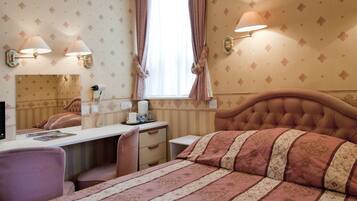 Een hotelkamer met een bed, een bureau, een stoel, een spiegel en een raam met gordijnen.