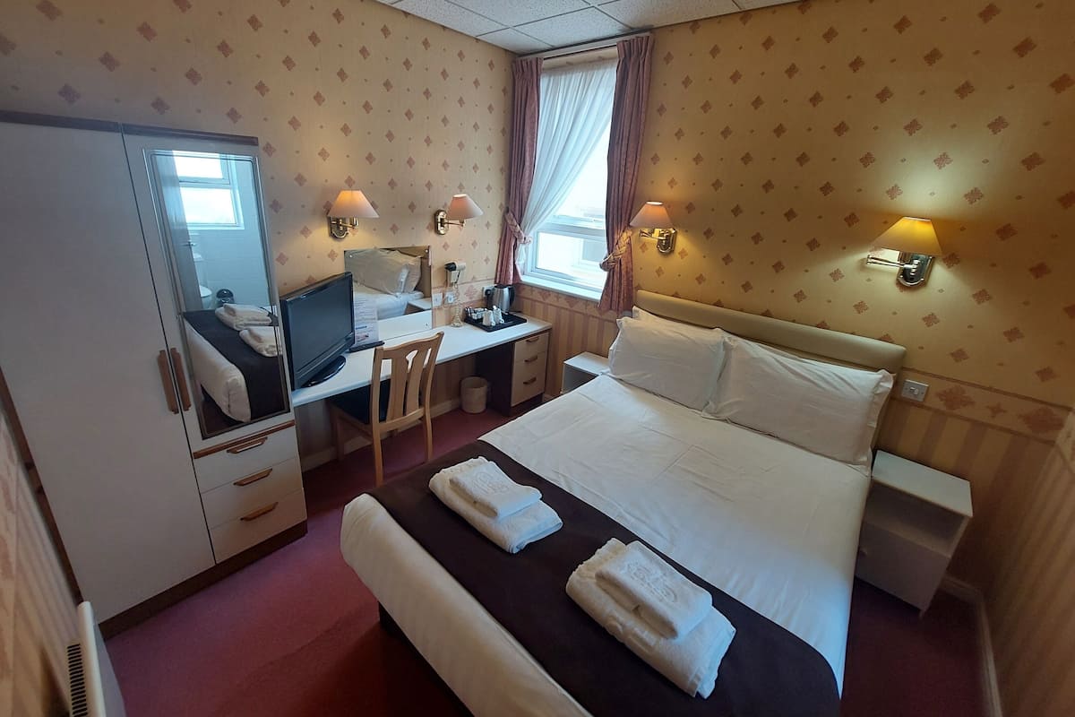 A hotel room with a bed, desk, chair, and a wardrobe.