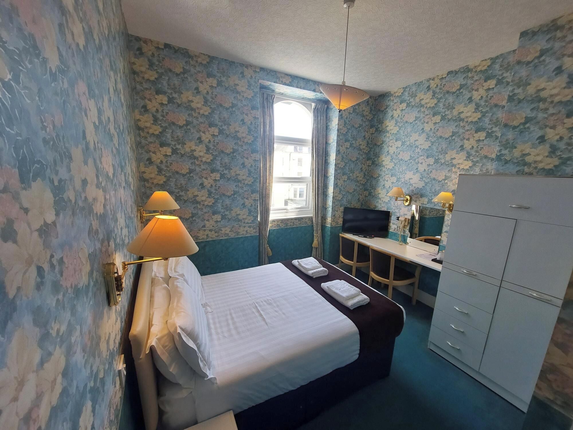 A hotel room with a bed, desk, TV, and wardrobe.
