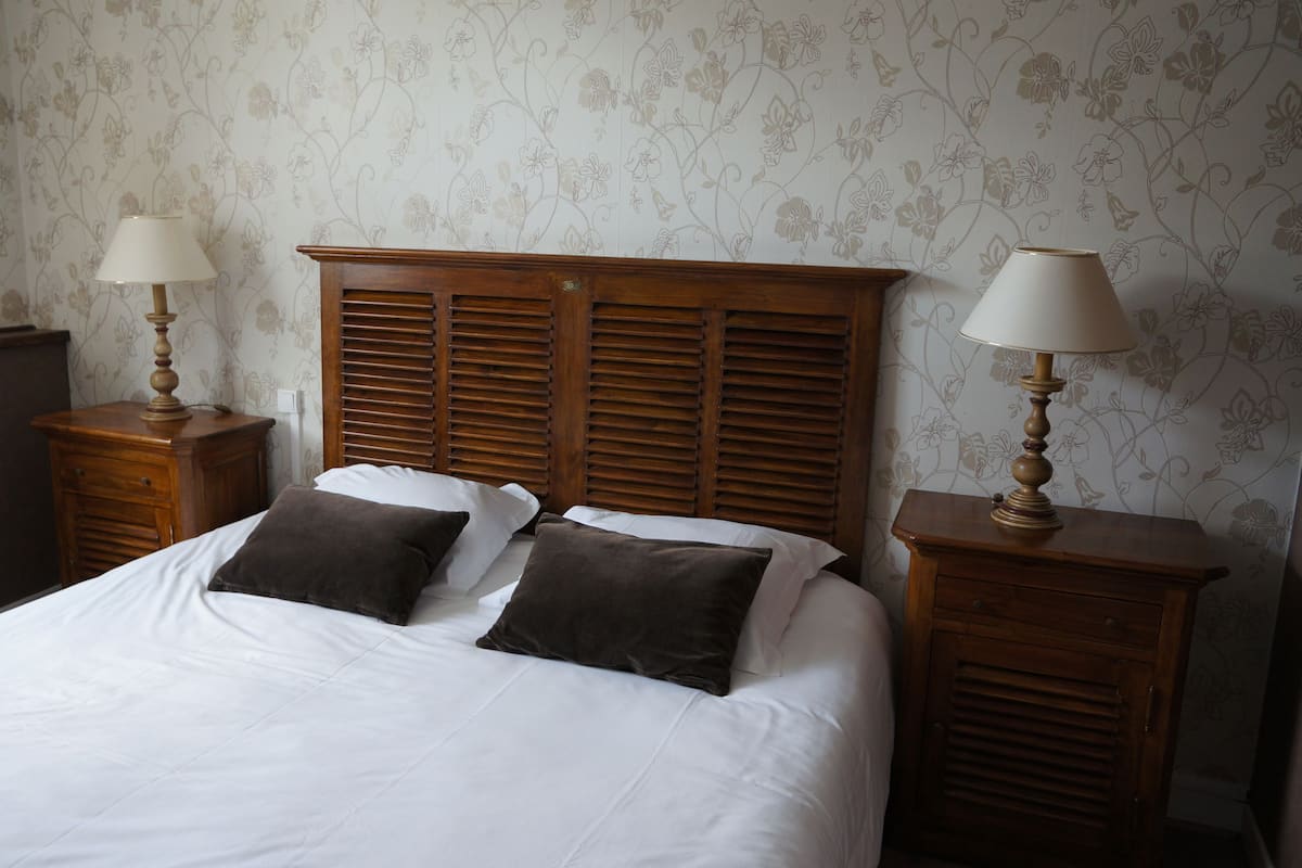 A neatly made bed with two pillows, flanked by wooden nightstands with lamps, against a floral wallpaper background.