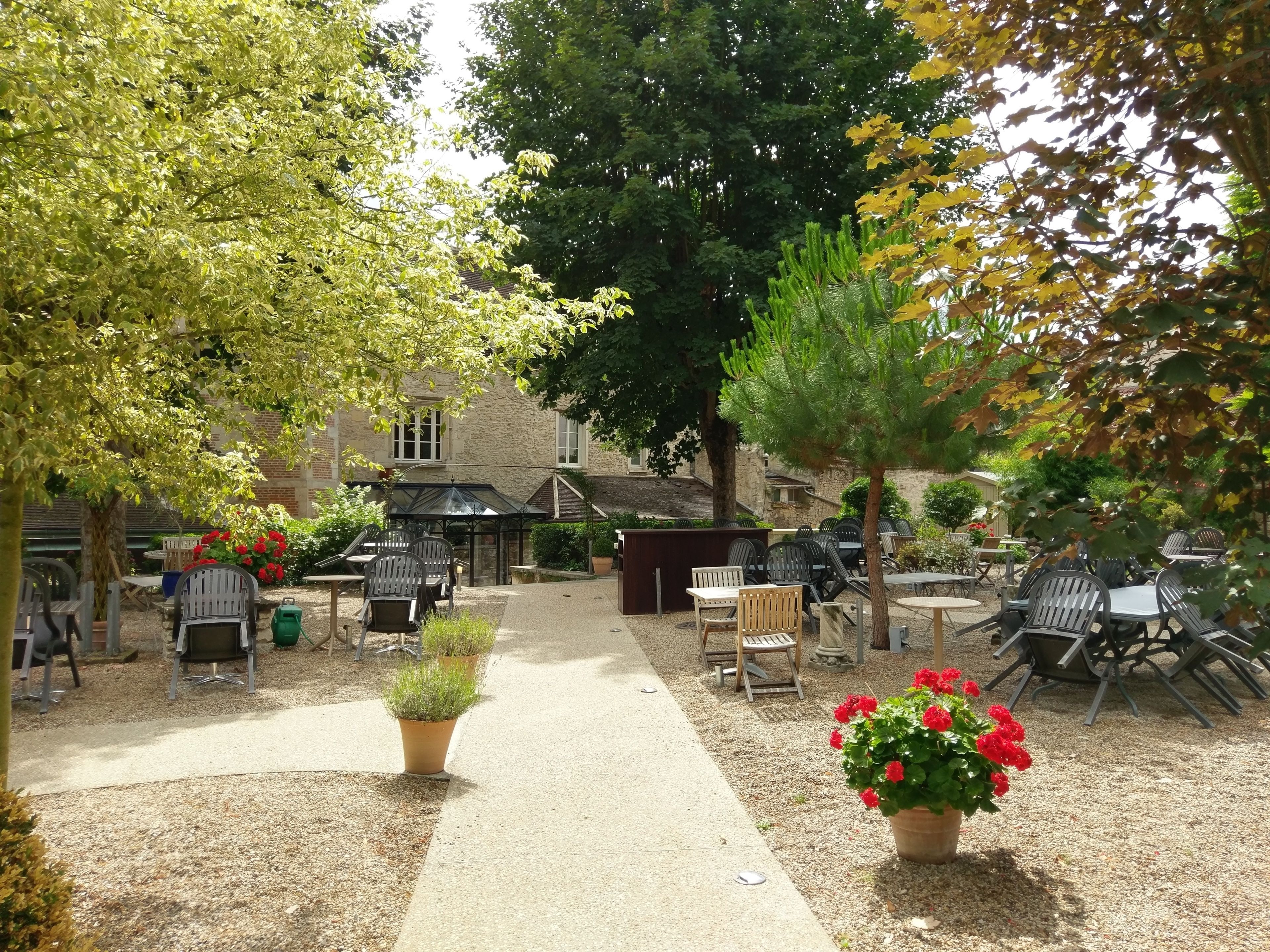 An outdoor seating area with tables and chairs, surrounded by trees and a building in the background.