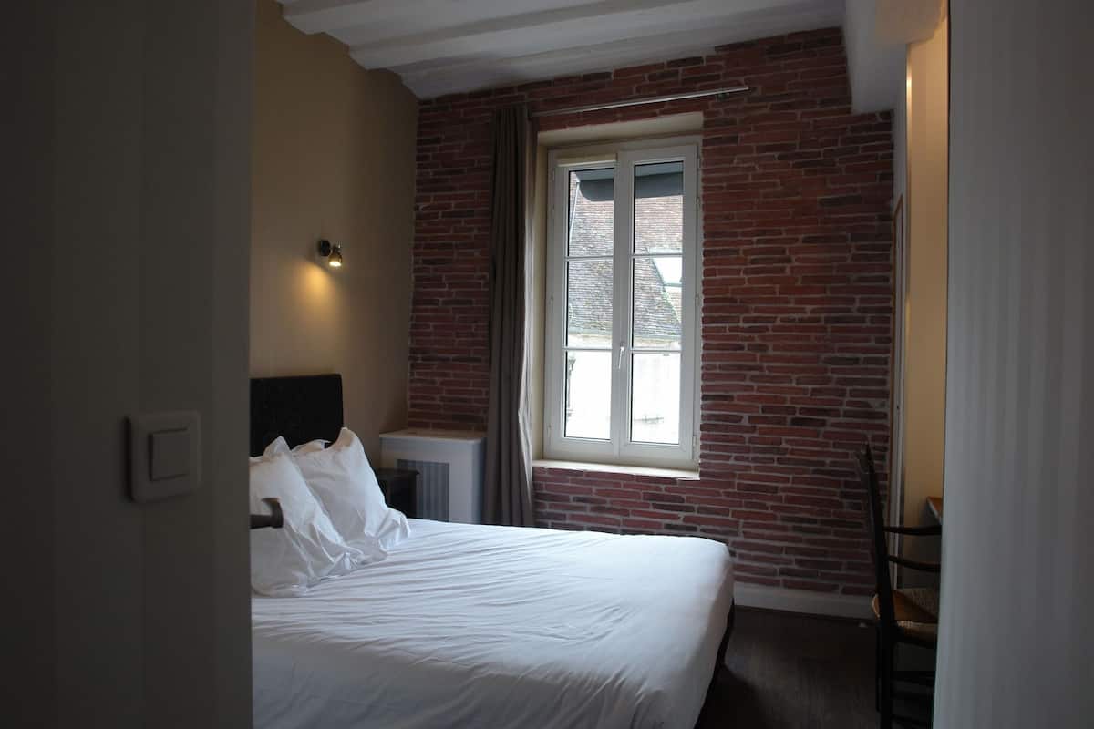 A bedroom with a brick wall, a window, a bed, and a chair.