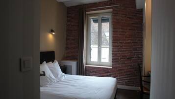 Een slaapkamer met een bakstenen muur, een raam, een bed en een stoel.