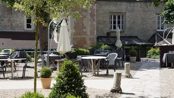 An outdoor patio with tables and chairs, surrounded by stone walls and greenery.