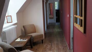A narrow hallway with wooden flooring, a red wall, and a window on the left.