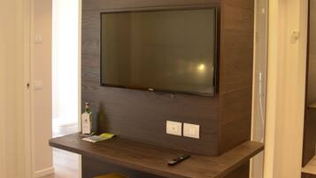 Una sala de estar moderna con un televisor de pantalla plana grande montado en una pared de madera oscura. Hay un otomano amarillo en primer plano y un control remoto sobre el mueble de televisión.