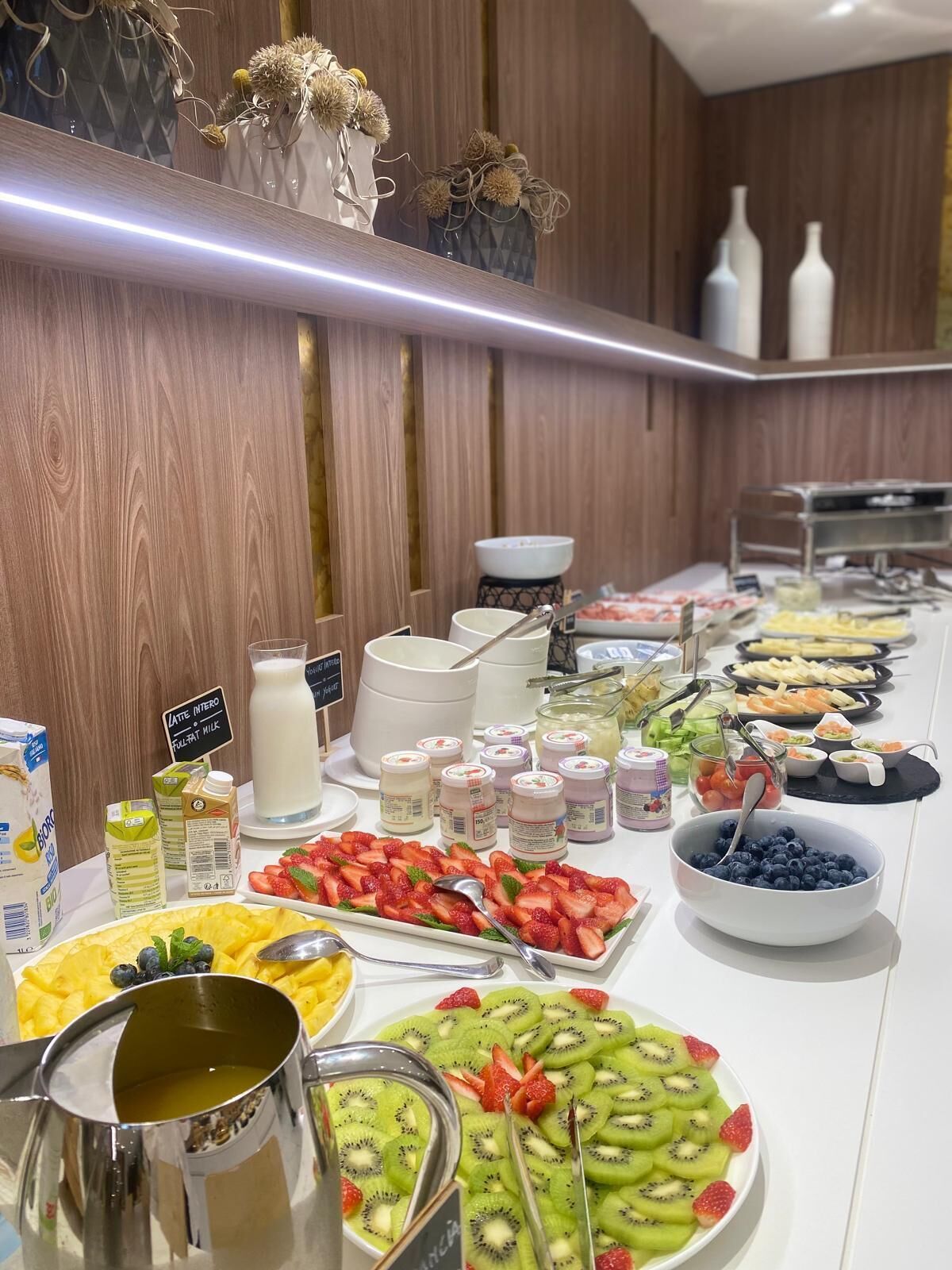 A buffet with various food items and beverages, including fruits, yogurt, and milk.