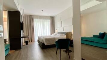 Ein modernes Hotelzimmer mit Bett, Schreibtisch, Sessel, Sofa und einem großen Spiegel.