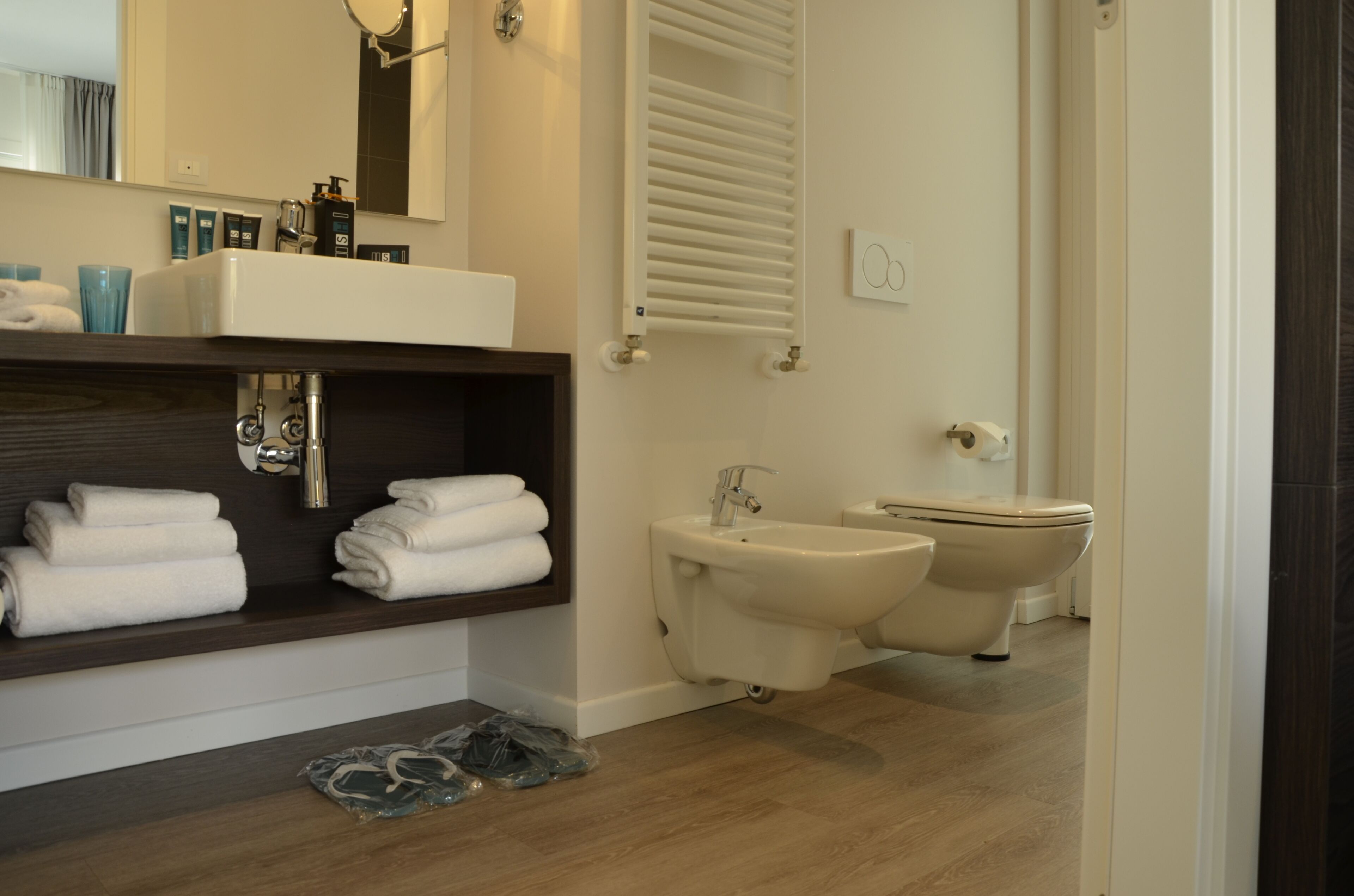 Un baño moderno con lavamanos, bidé e inodoro. Hay toallas en un estante y artículos de aseo en la encimera.