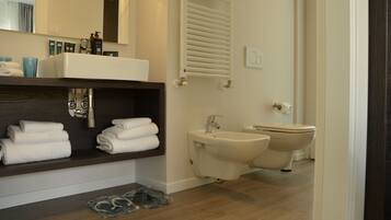 Un baño moderno con lavamanos, bidé e inodoro. Hay toallas en un estante y artículos de aseo en la encimera.