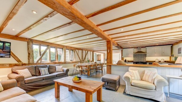 A spacious living area with a wooden ceiling, a sofa set, a dining table, and a kitchen area. - Butley Barn (Woodbridge)