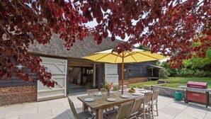 An outdoor patio with a wooden table set for dining, a yellow umbrella, and a barbecue grill. - Butley Barn (Woodbridge)