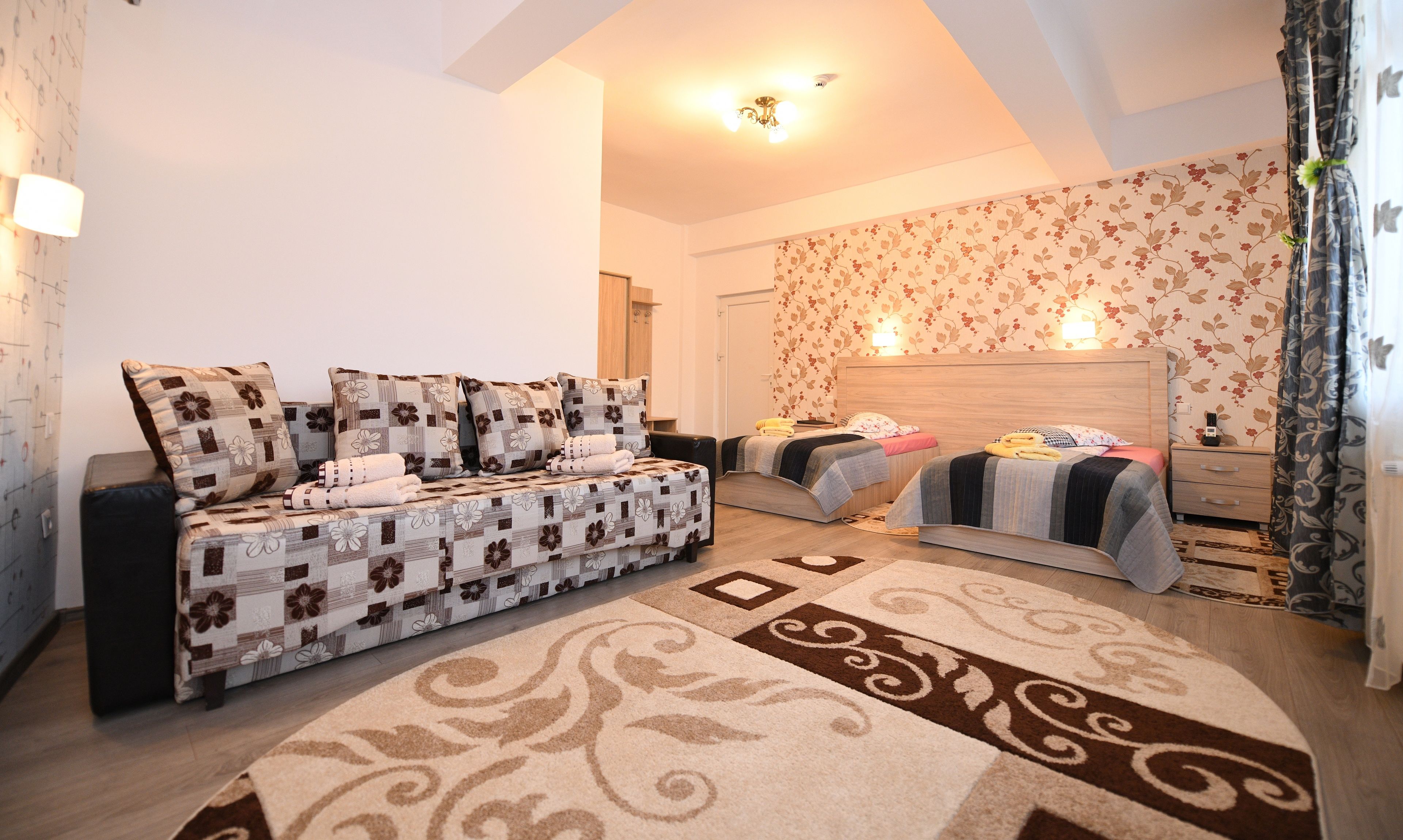 Ein Schlafzimmer mit einer Couch, zwei Betten, einem hölzernen Kopfteil und einer Wand mit Blumenmuster.
