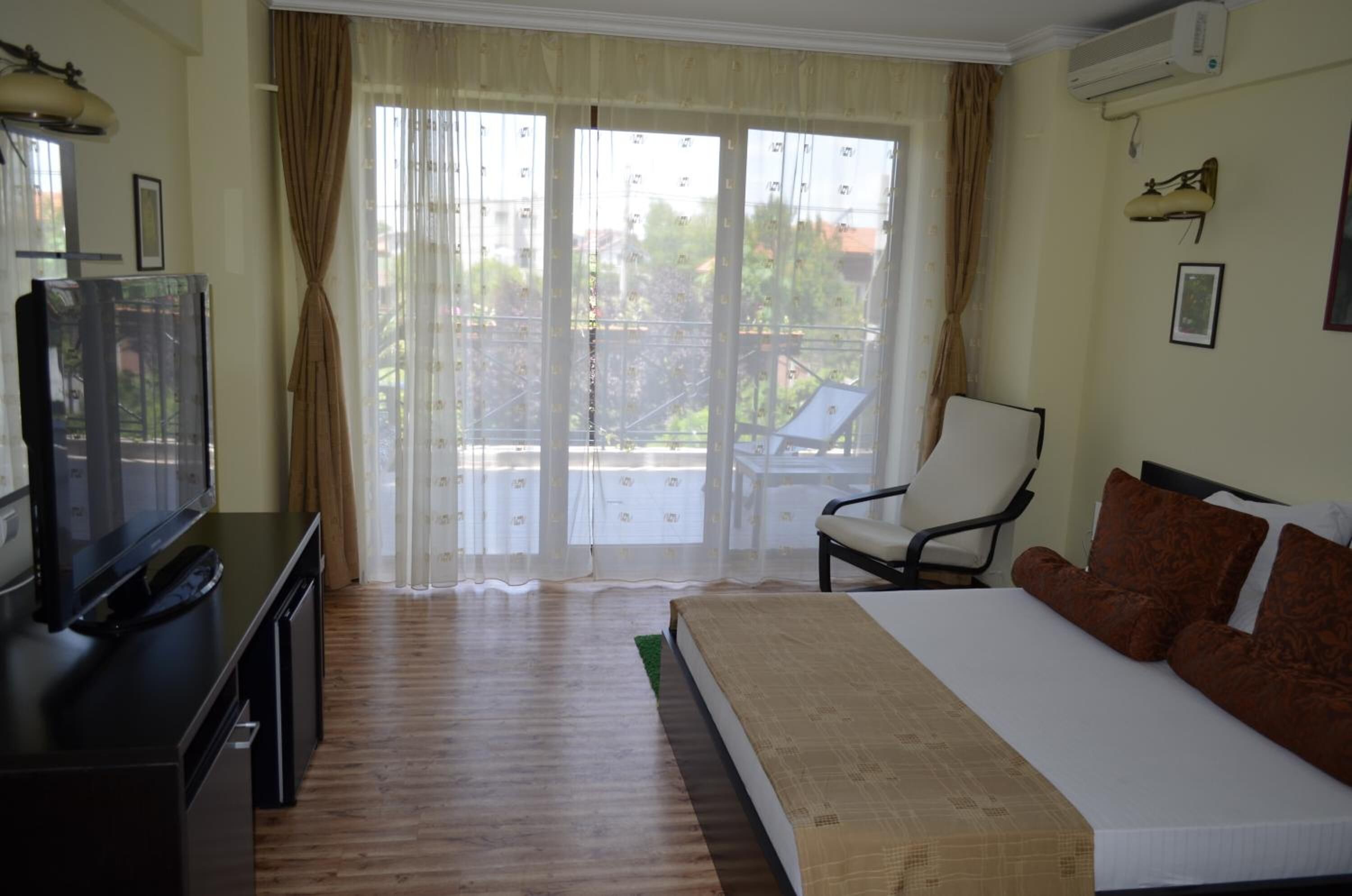 Ein Hotelzimmer mit Bett, Fernseher, Sessel und einem Balkon mit Vorhängen.