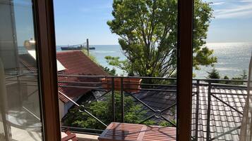 A balcony with a table and chairs, overlooking a coastal area with a bridge and trees.