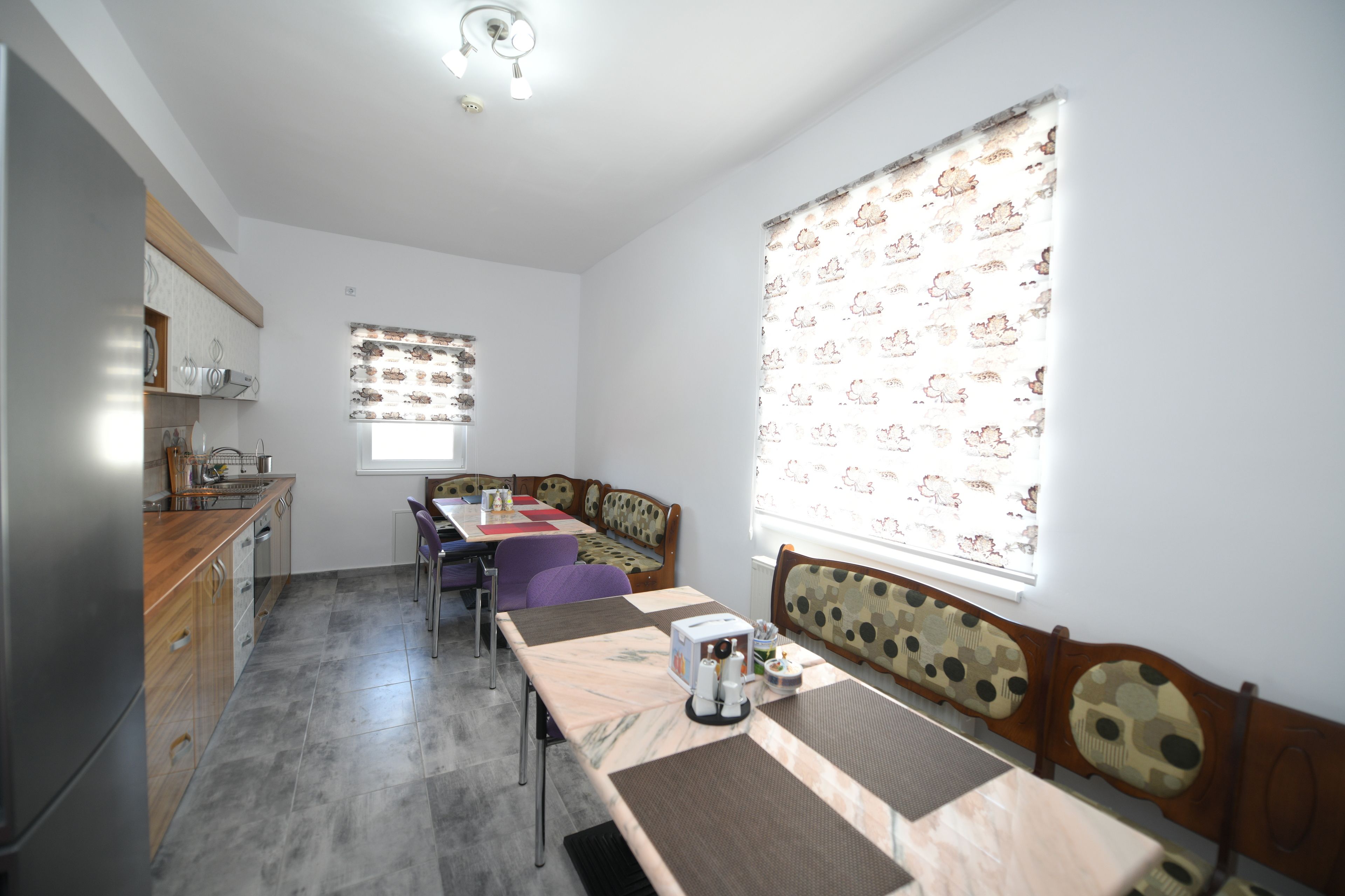 Una cocina moderna con comedor, que incluye una mesa larga y sillas, y un ventanal con cortinas estampadas.