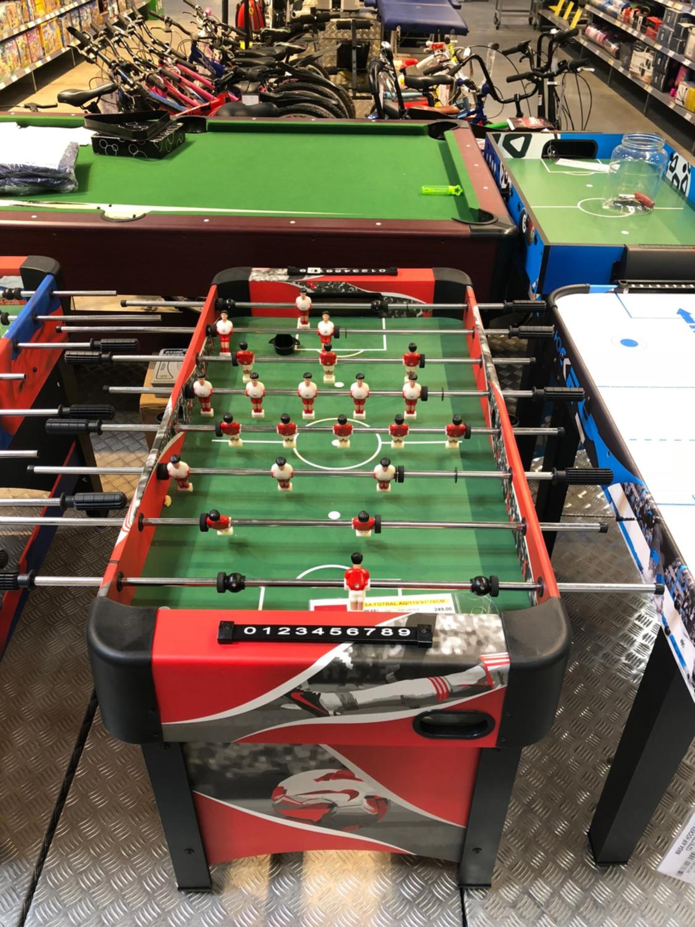 Una mesa de fútbol de mesa en una habitación con bicicletas y otros equipos deportivos al fondo.
