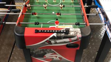 Una mesa de fútbol de mesa en una habitación con bicicletas y otros equipos deportivos al fondo.