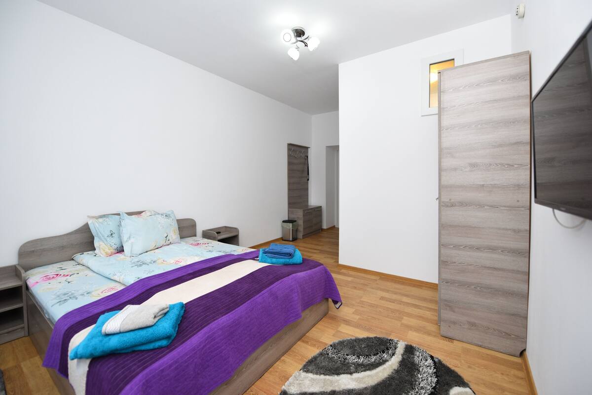 A modern bedroom with a bed, nightstands, a TV, and a wardrobe.