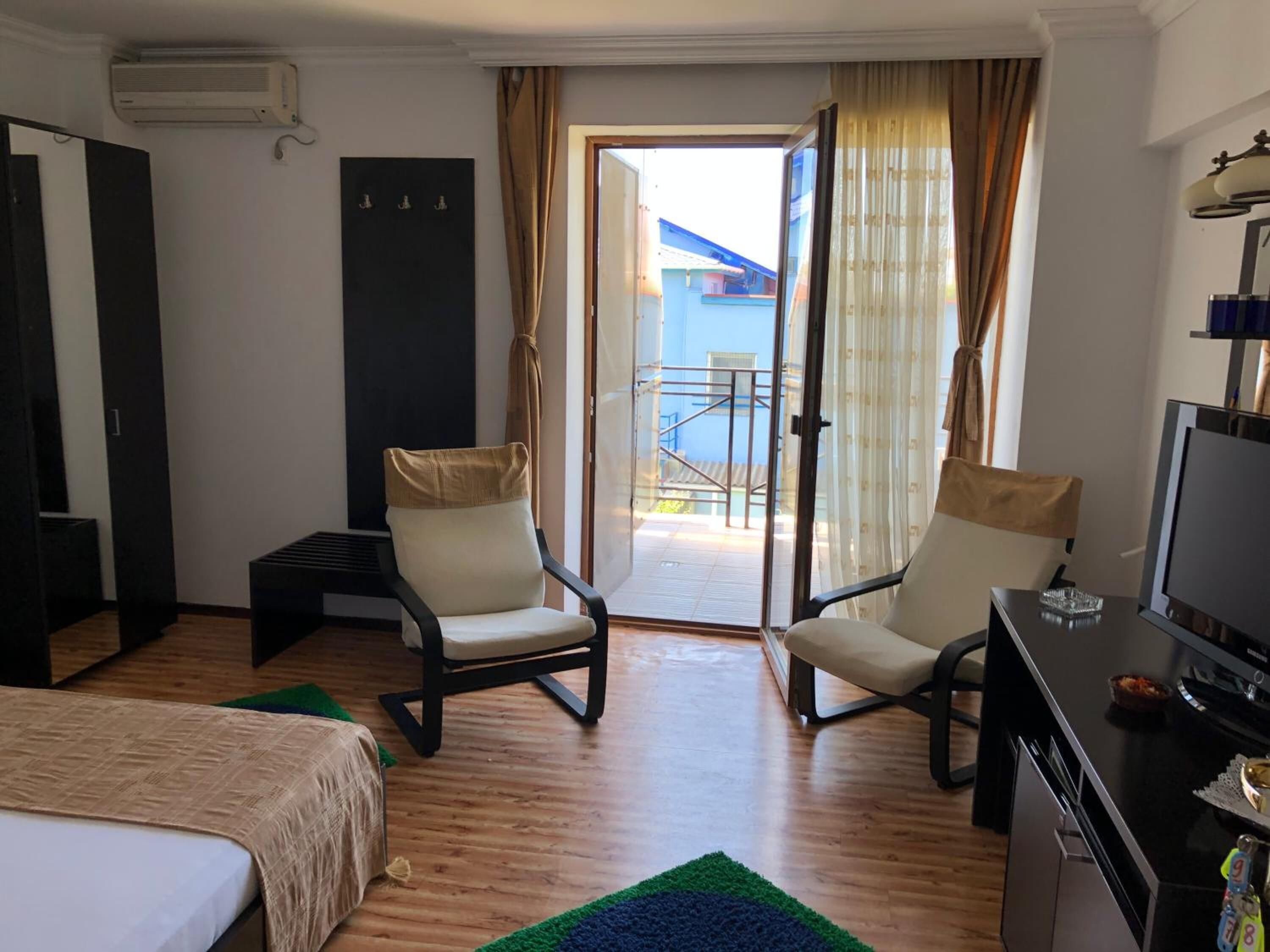 Habitación de hotel con cama, dos sillones, un escritorio con televisor, una mesita y balcón con vistas a edificios.