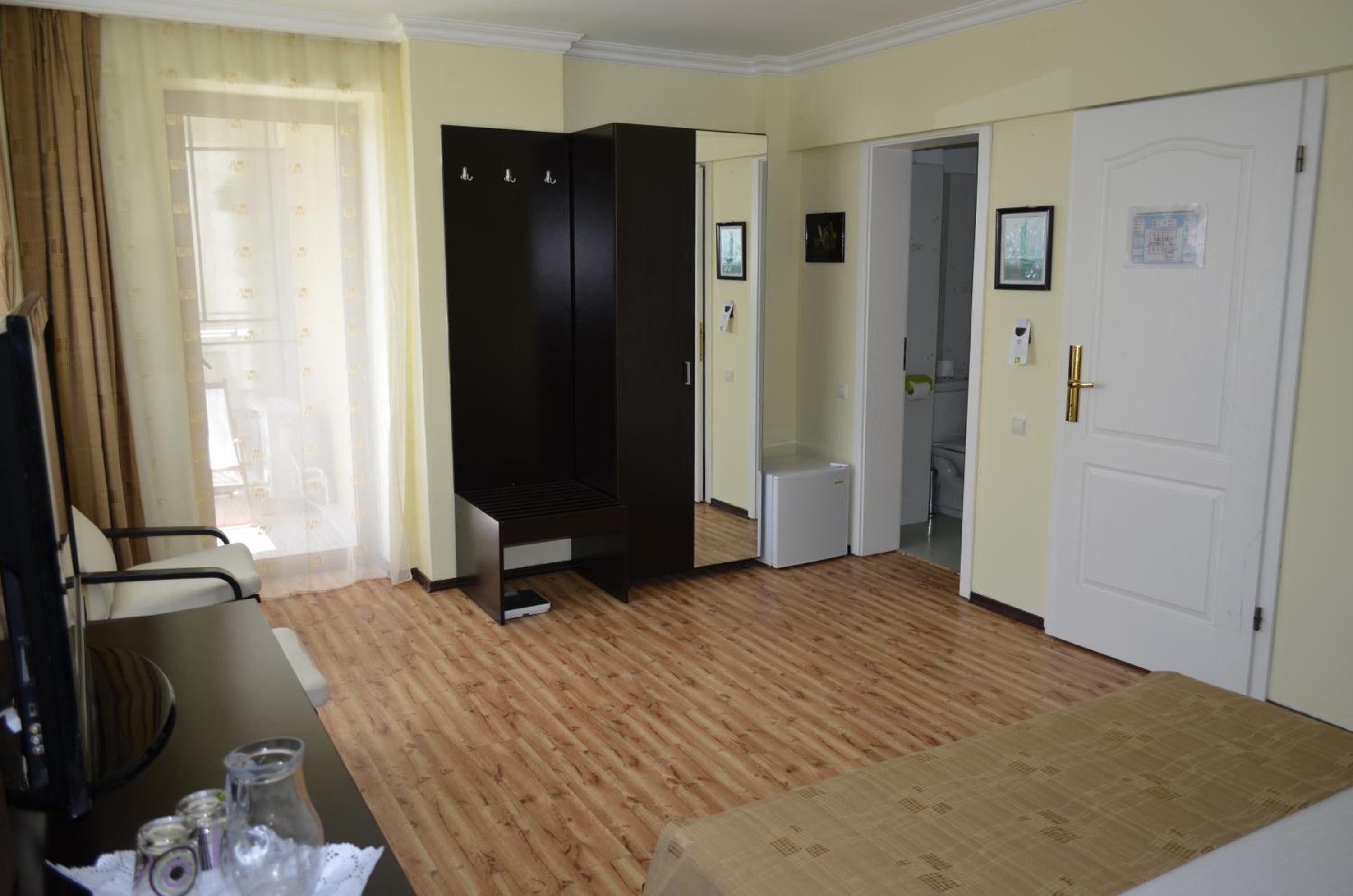 A hotel room with a bed, a desk, a wardrobe, a mirror, a door, and a window with curtains.