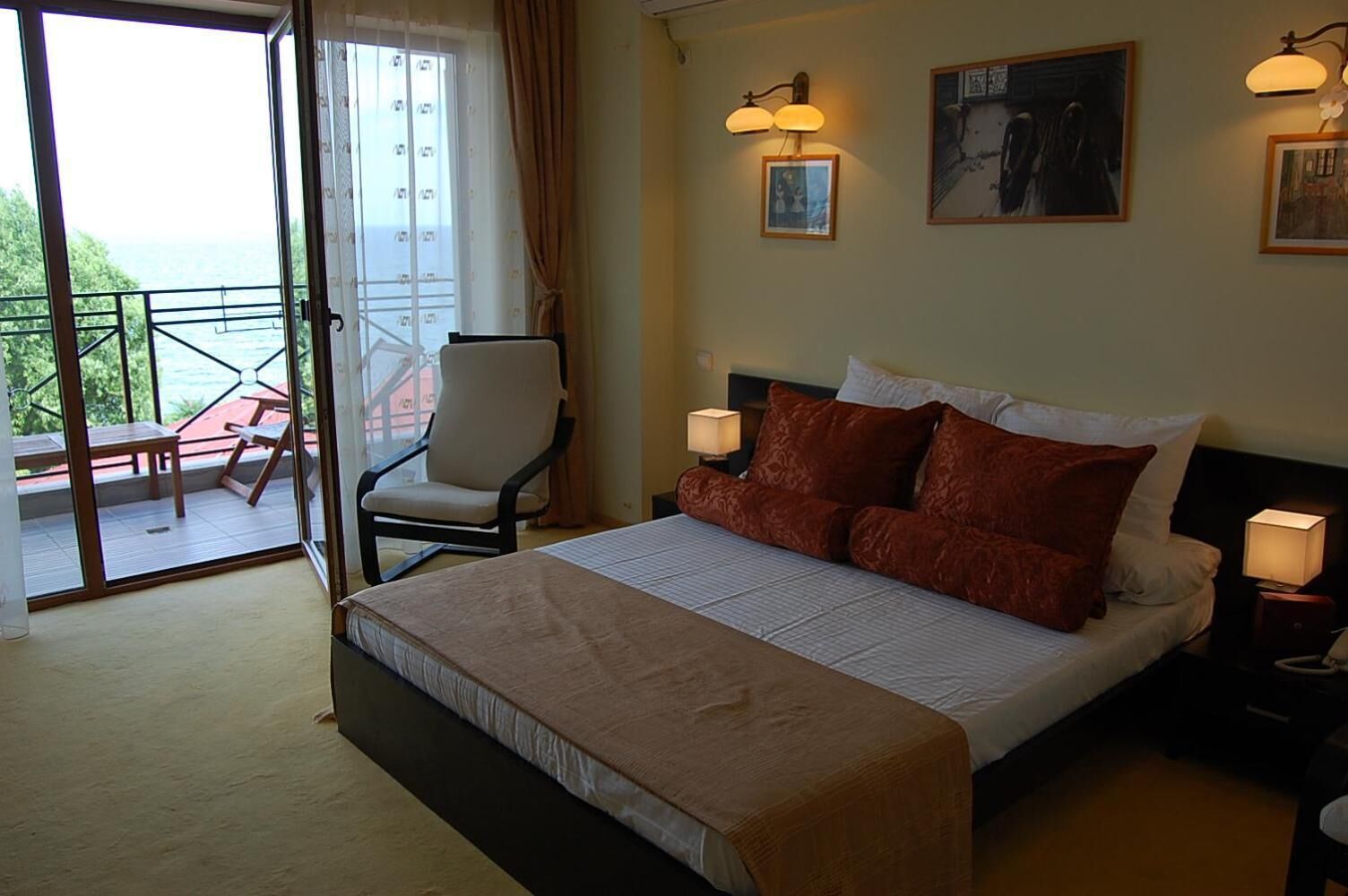 Una camera d'albergo con un letto, due lampade ai comodini, una sedia, un balcone con un tavolo e un quadro appeso al muro.
