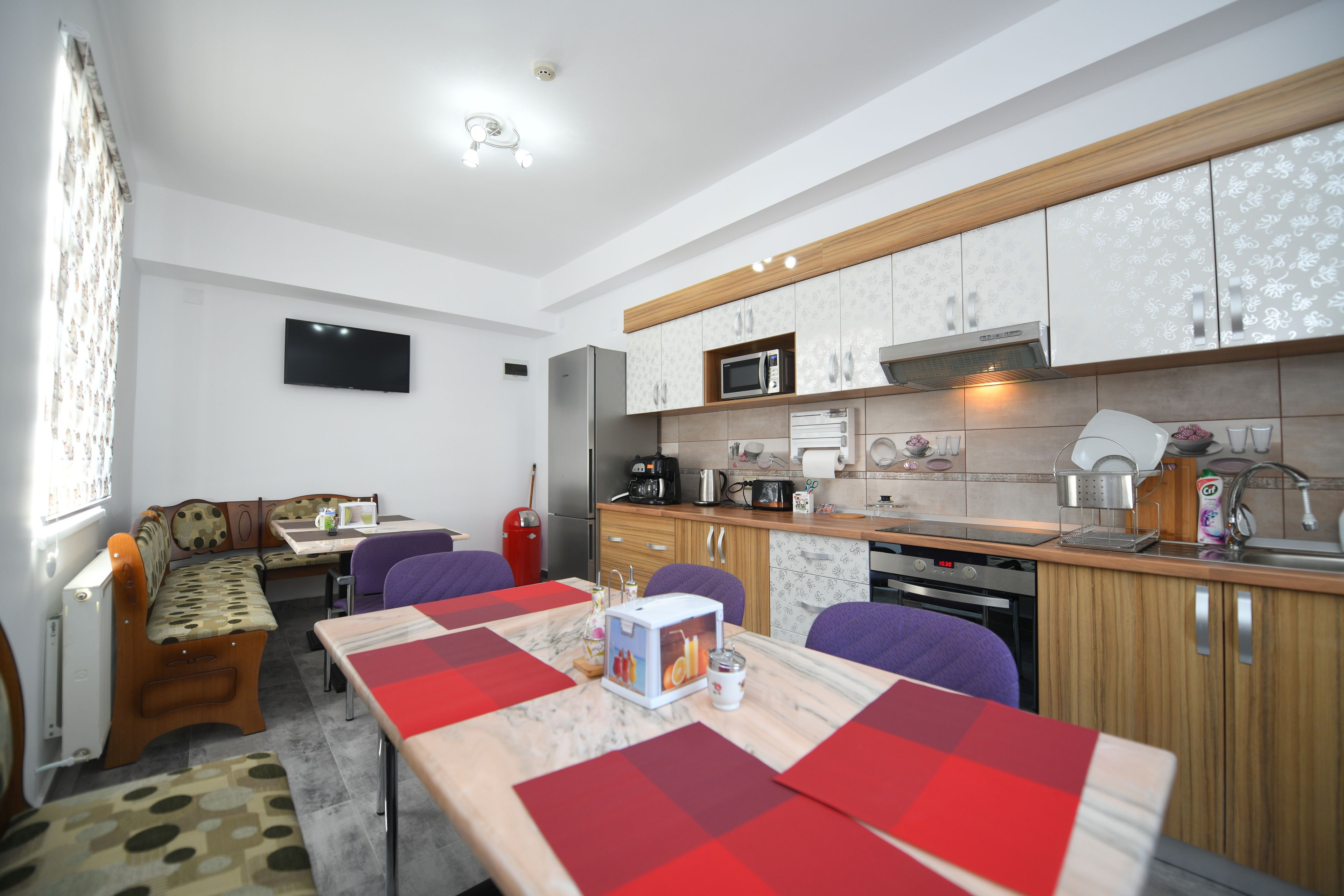 A compact kitchen with modern appliances, a dining area with a red tablecloth, and a seating area with a patterned bench.