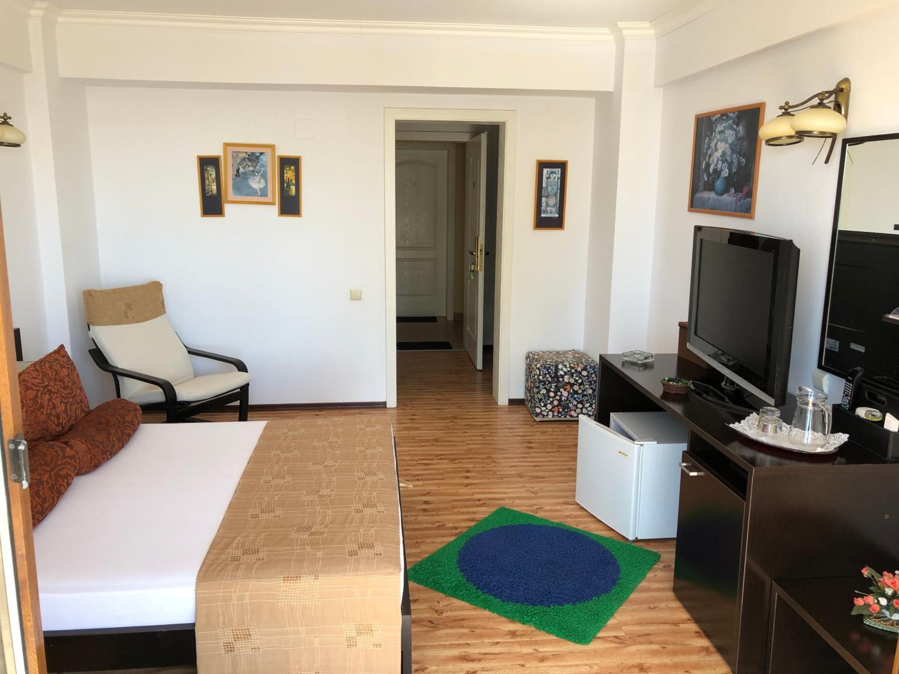 A compact hotel room with a bed, a chair, a desk with a TV, and a small kitchenette.