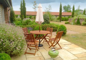 A patio with a round table and four chairs, a green grill, and an umbrella. - Lackford Lakes Barns (Bury St Edmunds)