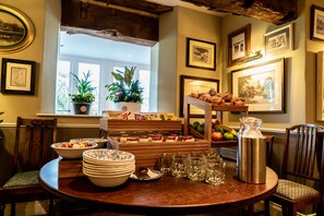 Buffet de l'esmorzar amb diferents aliments, una fornera de cafè i una finestra amb plantes.