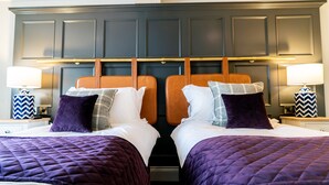 A hotel room with two beds, each with a headboard, and a nightstand with a lamp and decorative item.