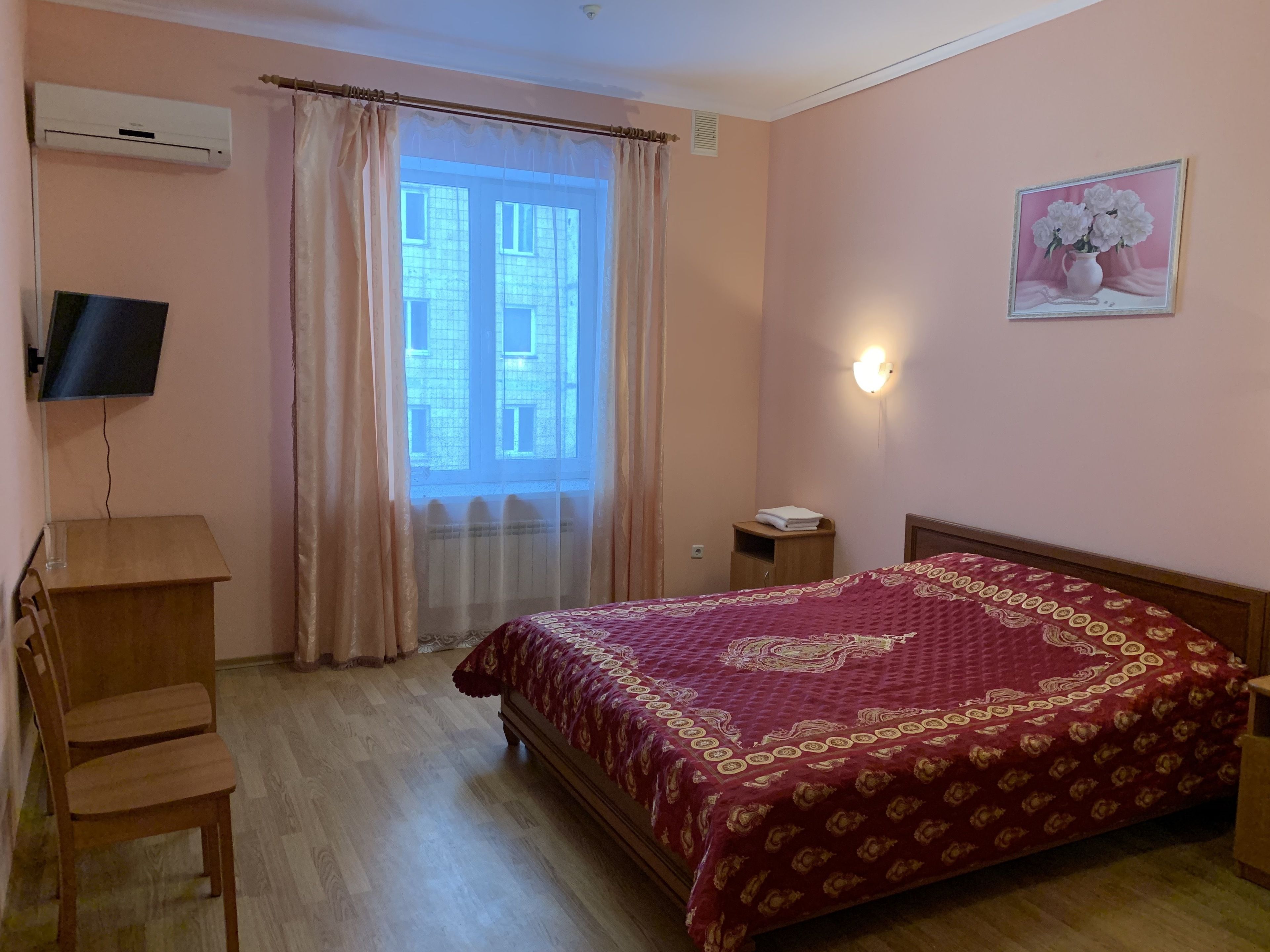 Een slaapkamer met een bed, een bureau, een stoel, een televisie en een raam met gordijnen.