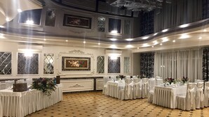 A spacious banquet hall with a checkered floor, multiple round tables set with white tablecloths and chairs, and decorative floral arrangements. - Inn on Zhytomyrska (Kyiv)