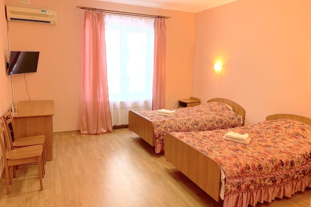 Een hotelkamer met twee bedden, een bureau, een stoel, een televisie en een raam met gordijnen.