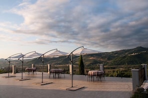 Une terrasse extérieure avec des tables et des chaises, une vue sur une montagne et un ciel nuageux.
