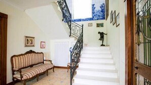 Eine Treppe mit schmiedeeisernem Geländer, eine weiße Wand mit gerahmten Bildern und ein gemusterter Boden.