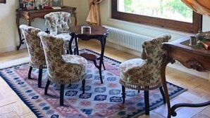 Ein Zimmer mit traditioneller Einrichtung, inklusive eines Holztisches, stühle mit Blumenmuster, einem gemusterten Teppich und Bildern an den Wänden.