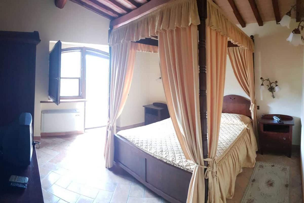 A bedroom with a four-poster bed, a bedside table, a nightstand, a window, and a television.